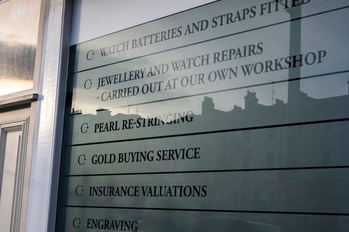 Storefront window with a gold-lettered list of jewelry and watch repair services, including engraving and valuations