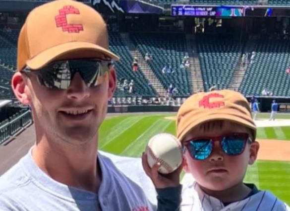 Two fans in orange caps and sunglasses holding a baseball in a stadium seat area