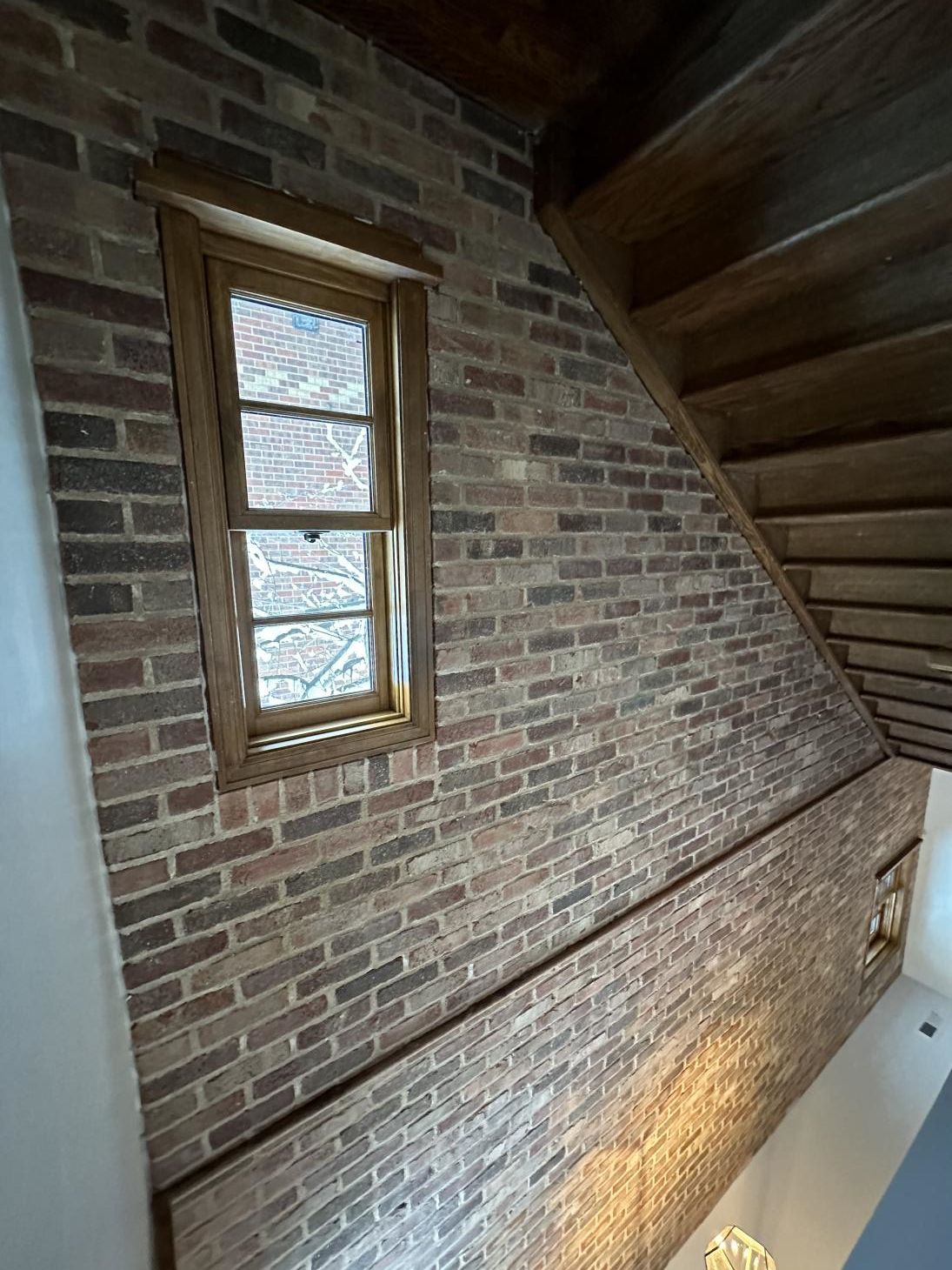 Brick wall and wooden staircase ceiling with a small window in an indoor stairwell
