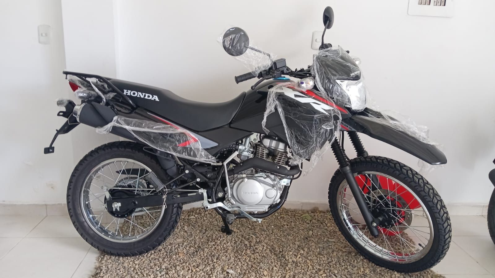 Motocicleta Honda negra y roja, vista lateral, en interiores. Envuelta en plástico.