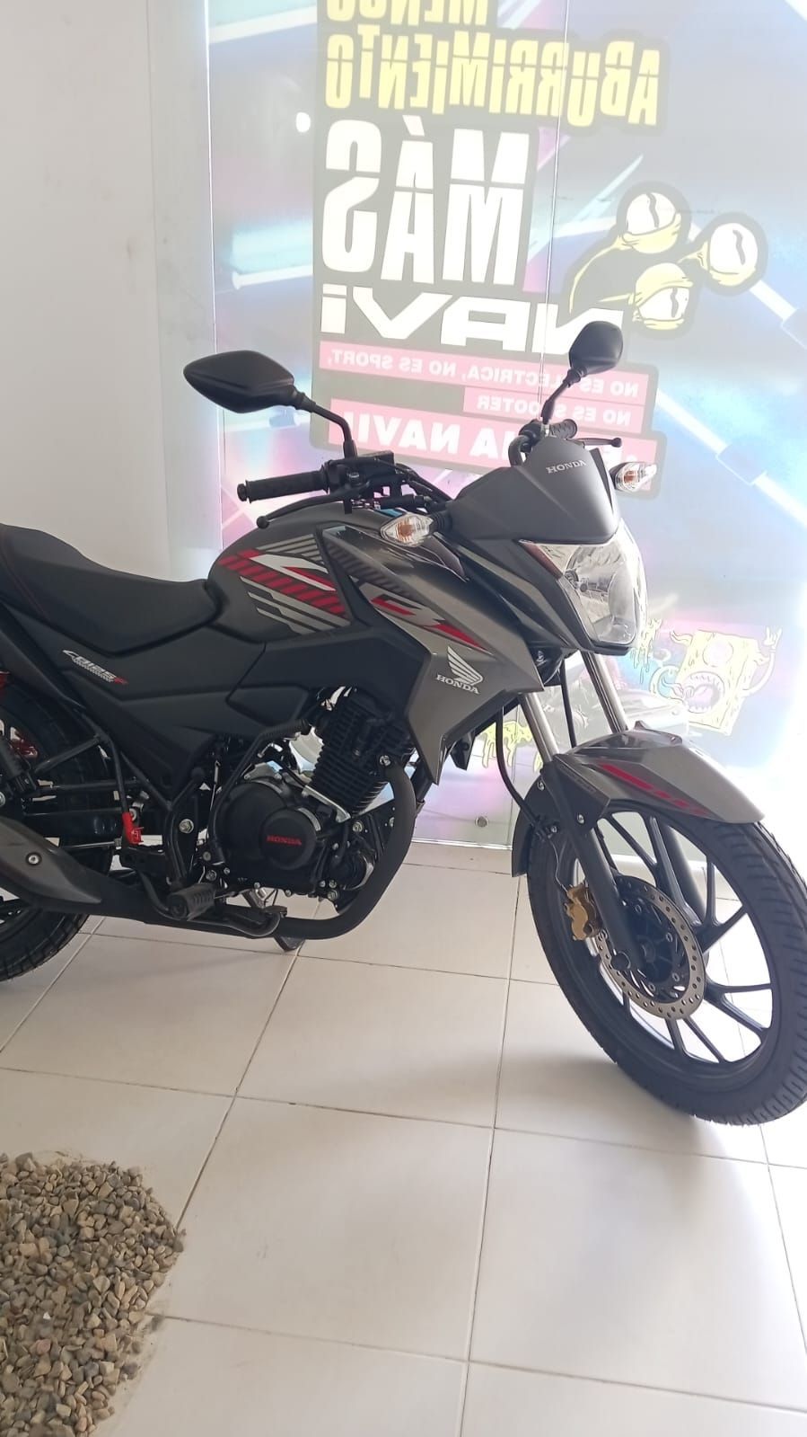 Motocicleta Honda de color gris y rojo estacionada en un lugar cerrado, con un escaparate al fondo.