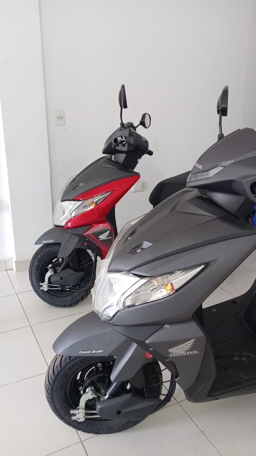 Dos scooters Honda Dio, rojo y gris, estacionados en el interior.
