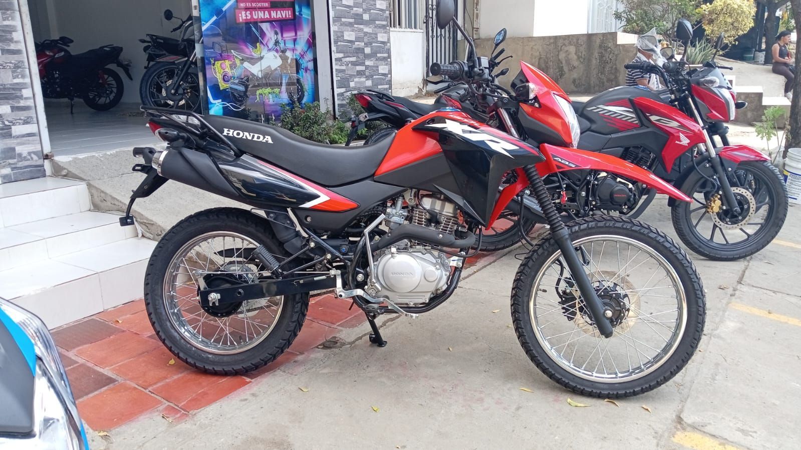 Motocicleta Honda roja y negra estacionada frente a un edificio con otra motocicleta roja.