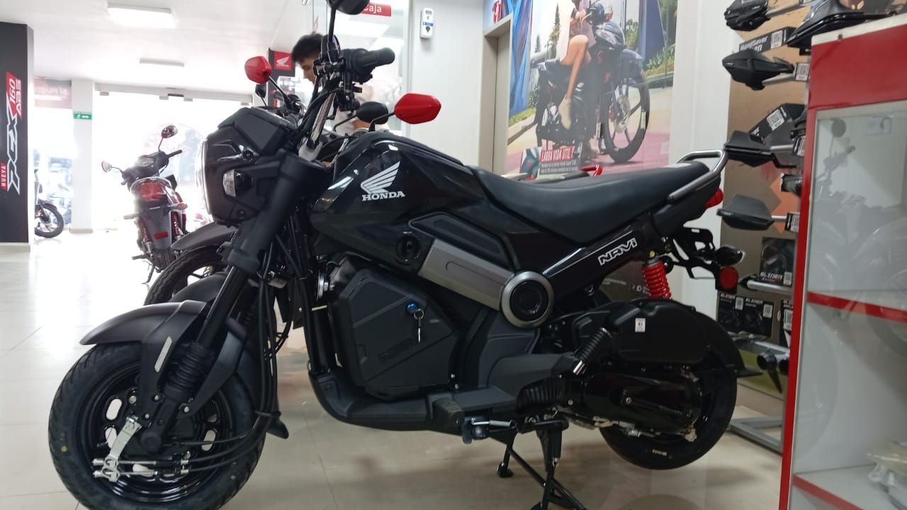 Motocicleta Honda Navi negra en exhibición en una sala de exposición, con accesorios visibles.