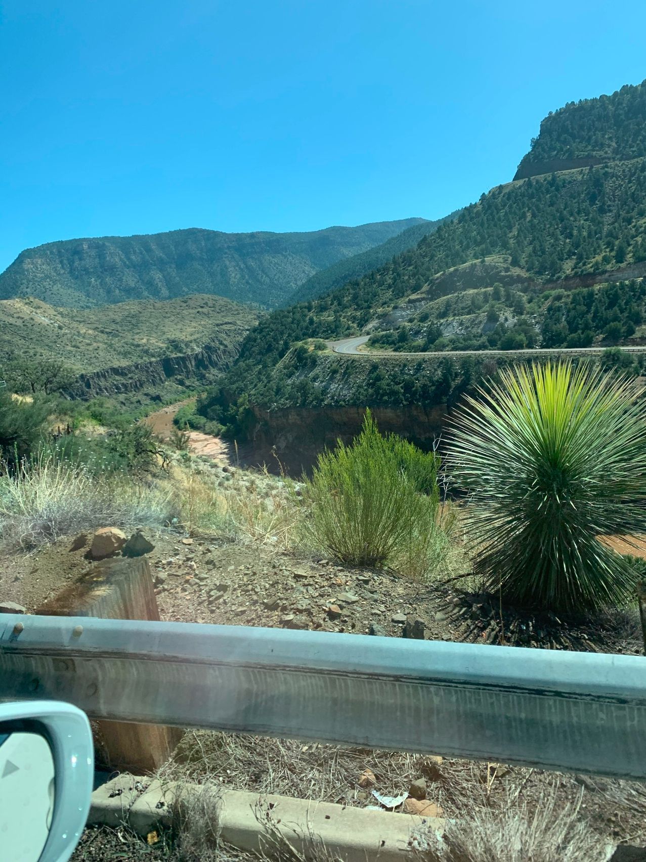 Mountains with a winding road, blue sky, and green and brown vegetation in a sunny environment.