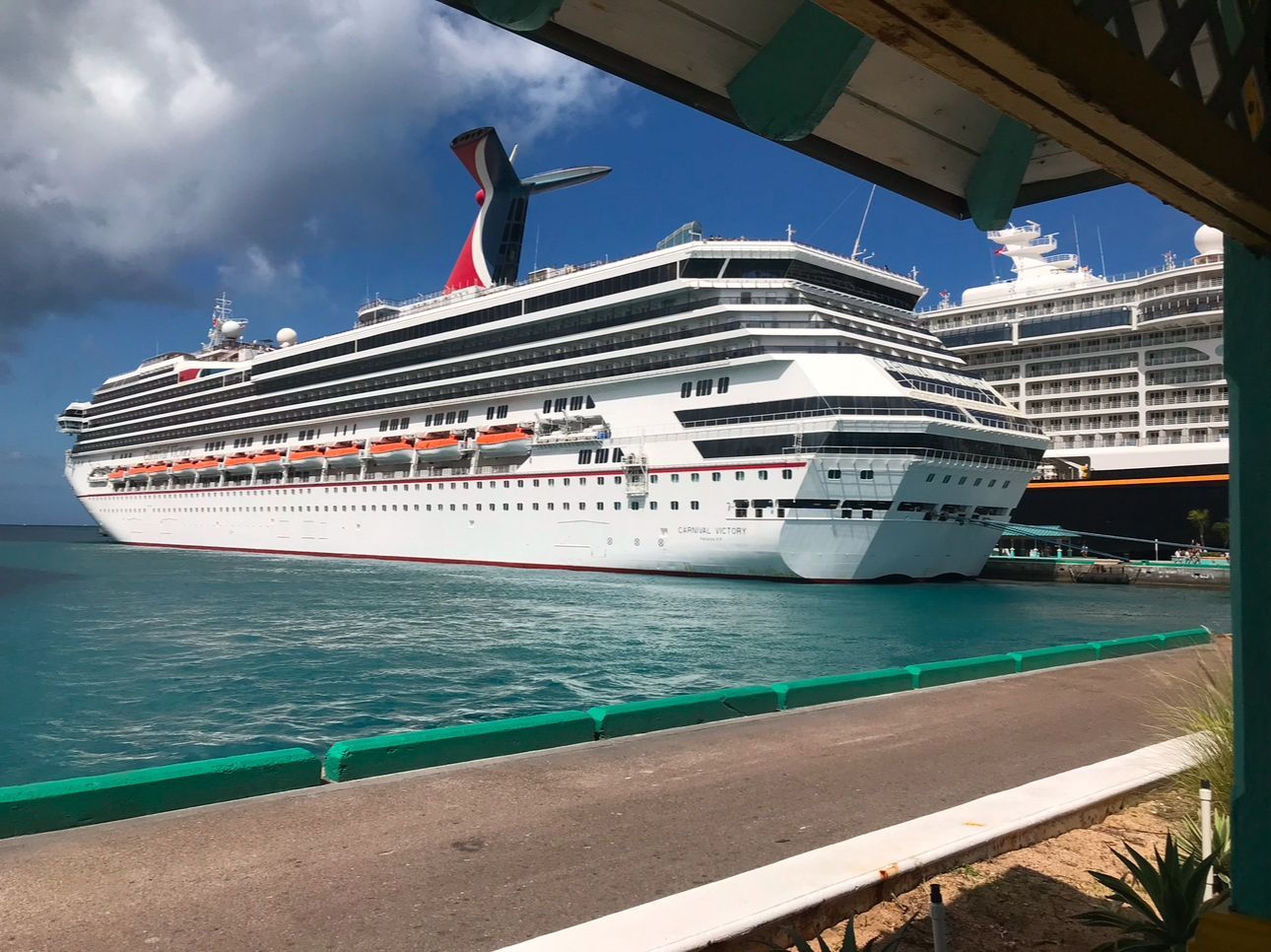 Large white cruise ship with red and blue accents docked in a turquoise harbor on a sunny day.