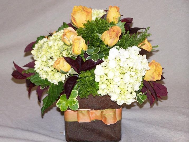 A vase filled with yellow roses and white hydrangeas
