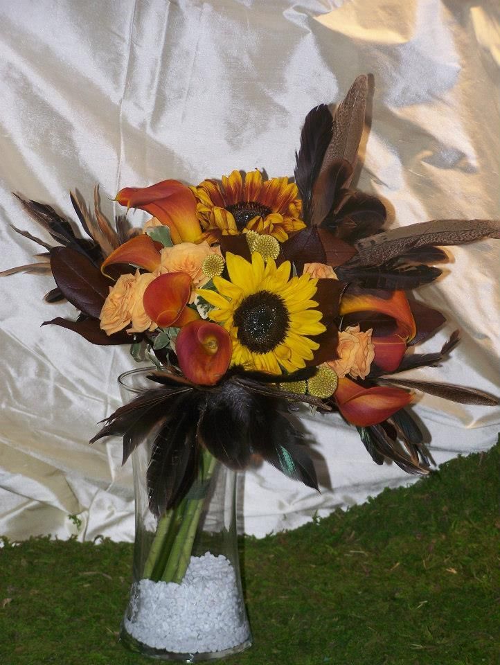 A vase filled with flowers including sunflowers and feathers
