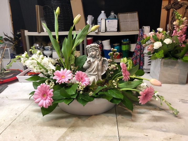 A white vase filled with pink and white flowers and a statue of an angel