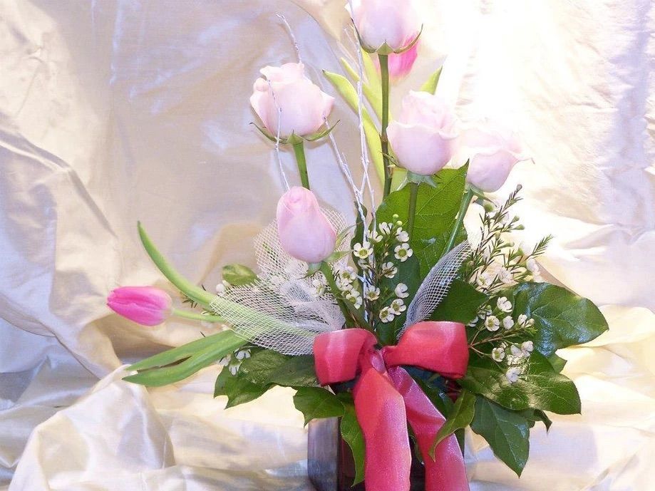A vase filled with pink and white flowers with a pink bow
