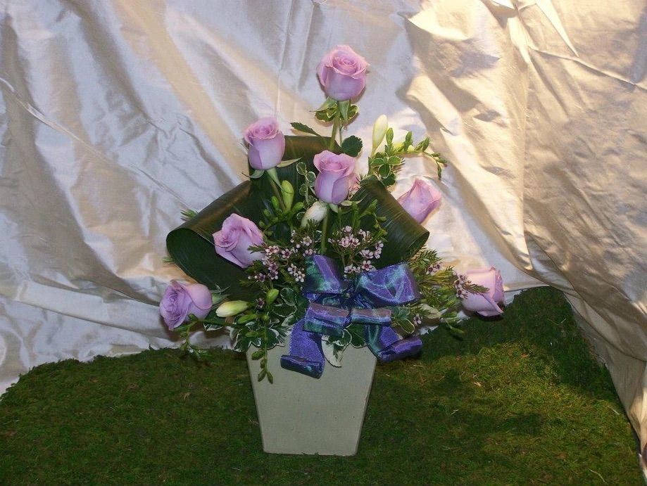A vase filled with purple roses and a purple bow