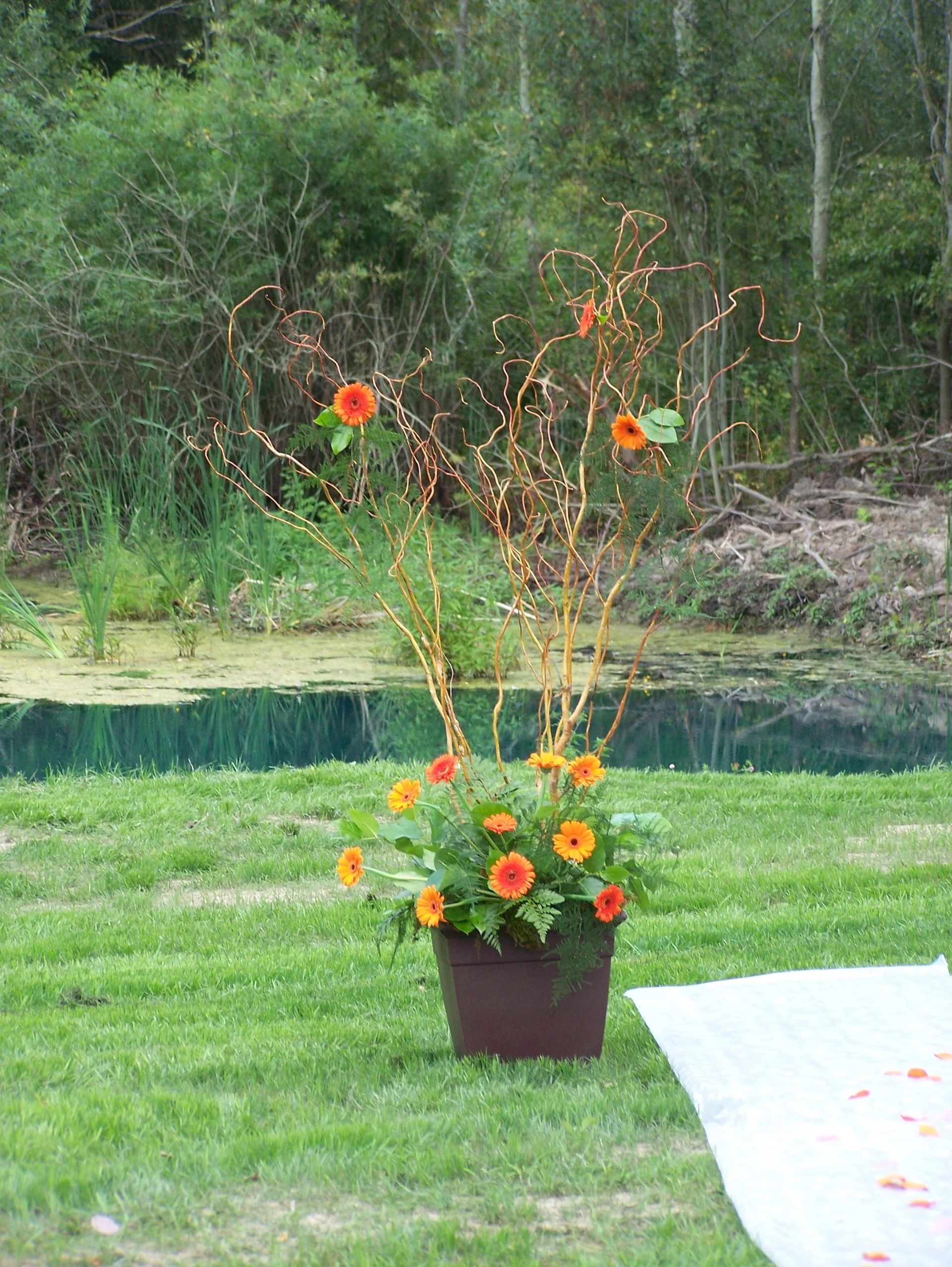 A vase filled with flowers is sitting in the grass in front of a pond.