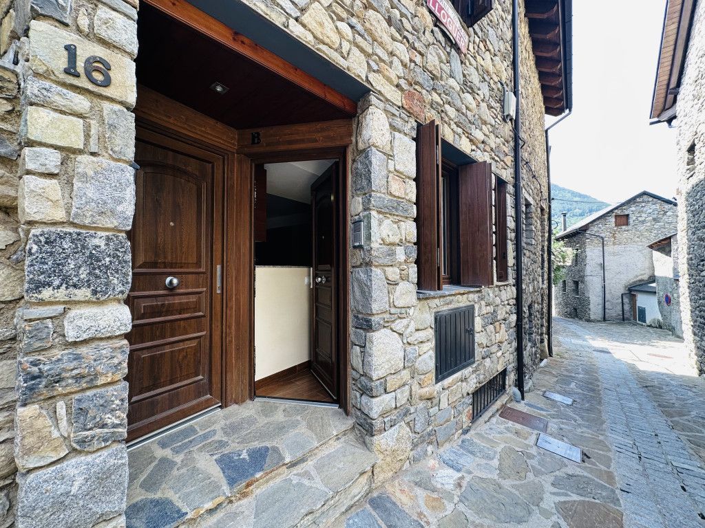 Edifici de pedra amb persianes marrons i un petit balcó contra un cel blau brillant.