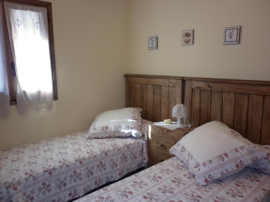 Llits individuals en una habitació amb roba de llit amb motius florals, tauleta de nit i una petita finestra.