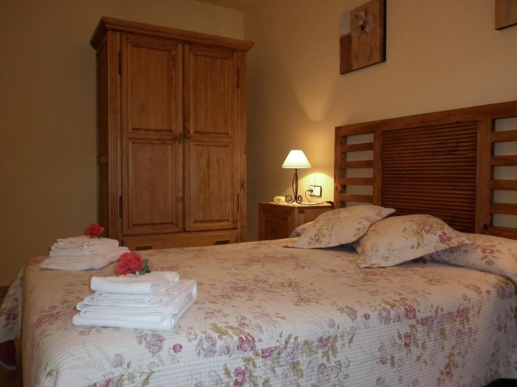 Dormitori amb mobles de fusta: llit amb roba de llit floral, tauleta de nit amb làmpada i armari.