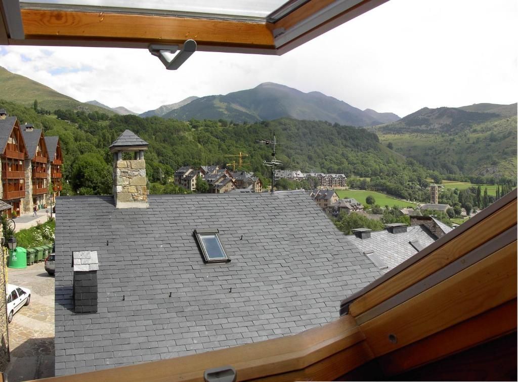 Vista des d'una finestra, amb vistes a un poble en una vall amb muntanyes al fons.