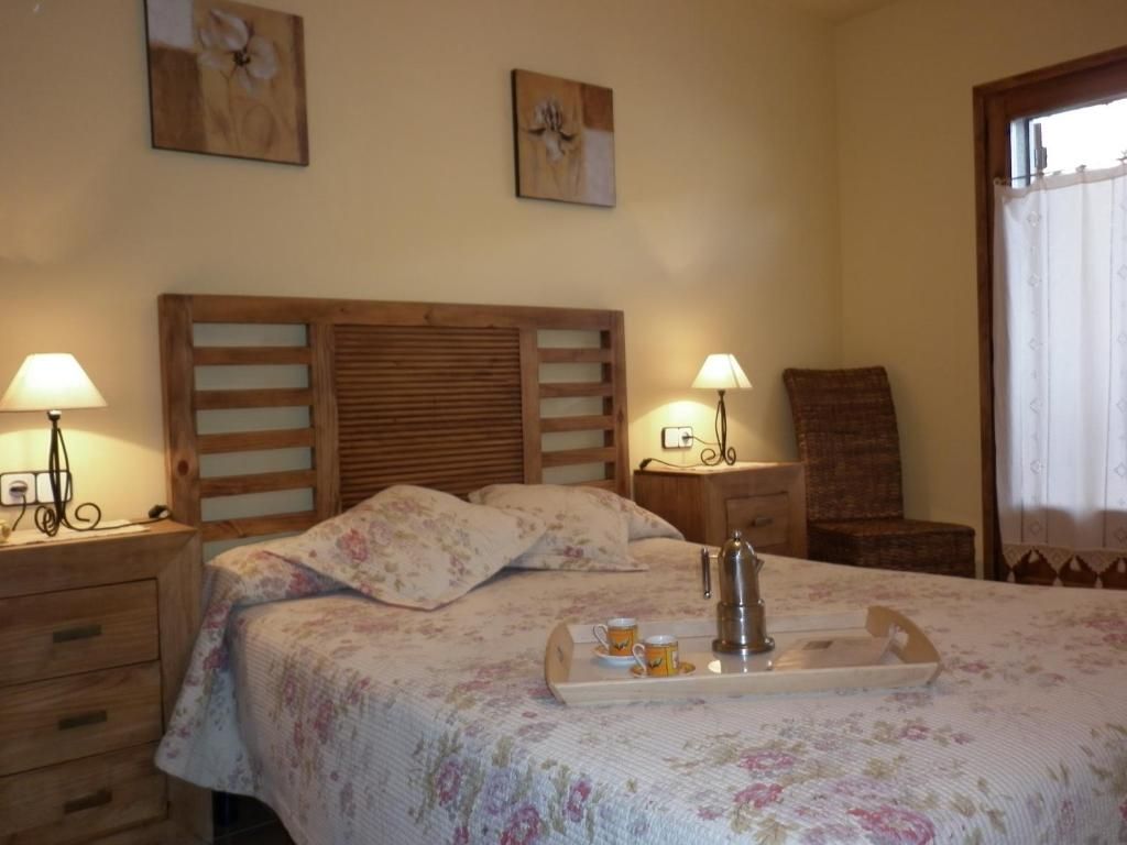 Dormitori amb marc de llit de fusta, edredó floral, tauletes de nit, làmpades i una safata amb cafè.