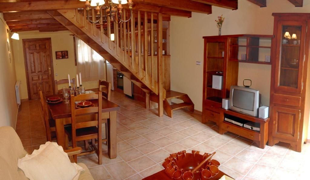 Sala d'estar amb mobles de fusta, escala, taula de menjador i terra de rajola.