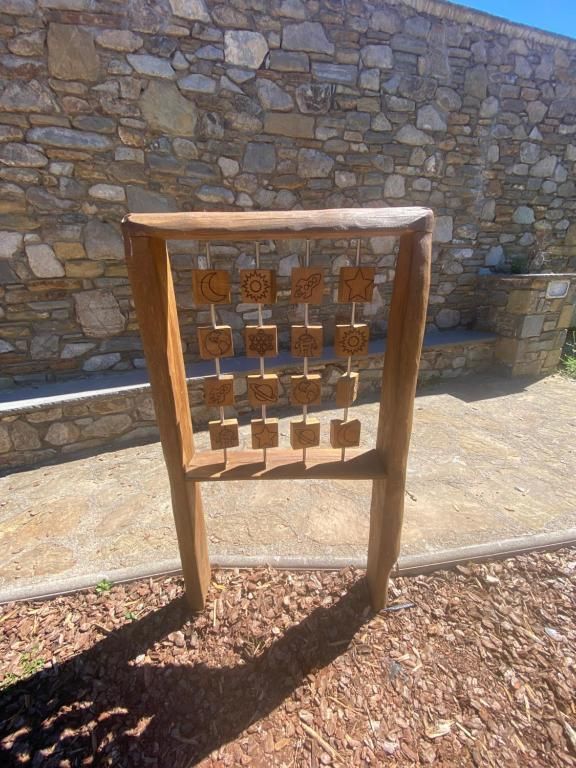 Peça d'art de fusta per a exterior amb elements quadrats de fusta i un fons de paret de pedra.