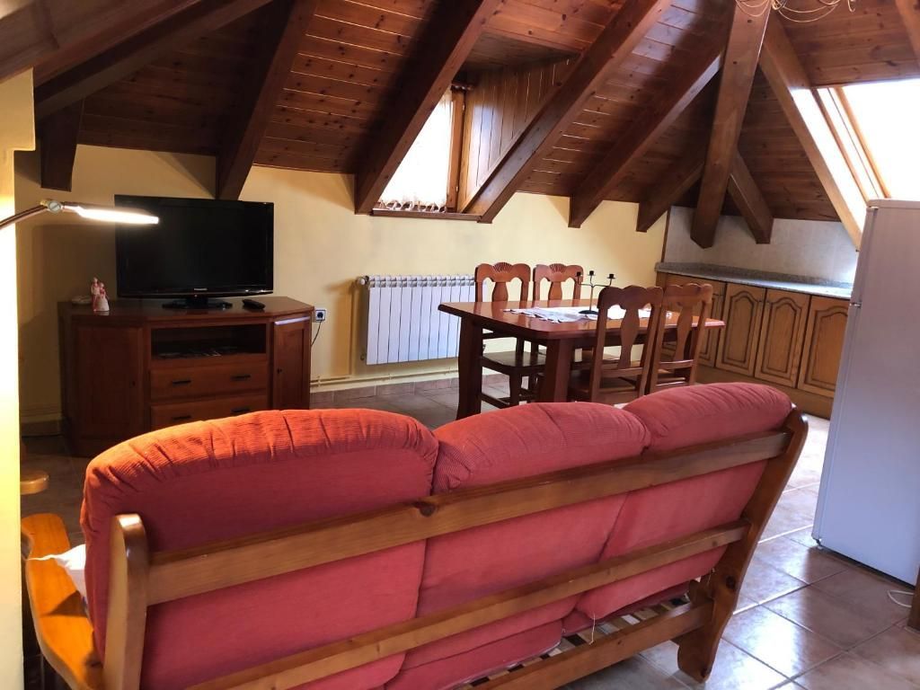 Sala d'estar amb sofà vermell, taula i cadires de fusta, televisor i sostre de fusta vista.