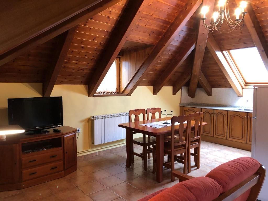 Acollidor apartament a l'àtic amb bigues de fusta a la vista, taula de menjador, cuina i TV.