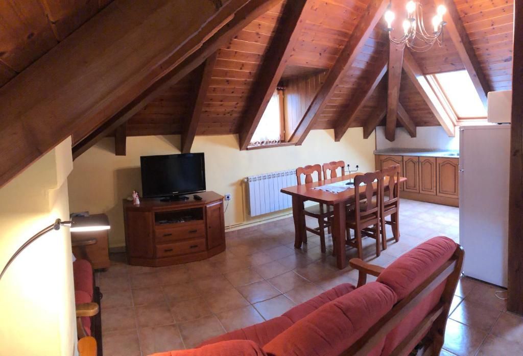 Pis tipus loft amb sostre de fusta inclinat, menjador i televisor en un armari de fusta.