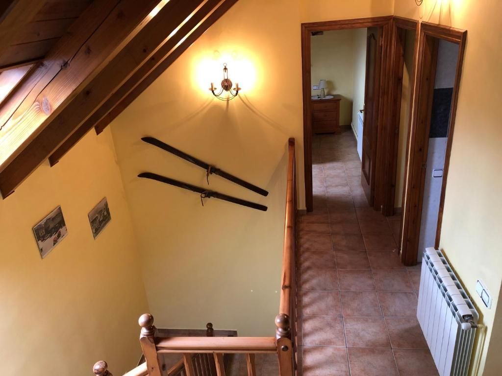 Passadís interior amb escales, parets grogues pàl·lides, bigues de fusta, dues portes i un radiador.