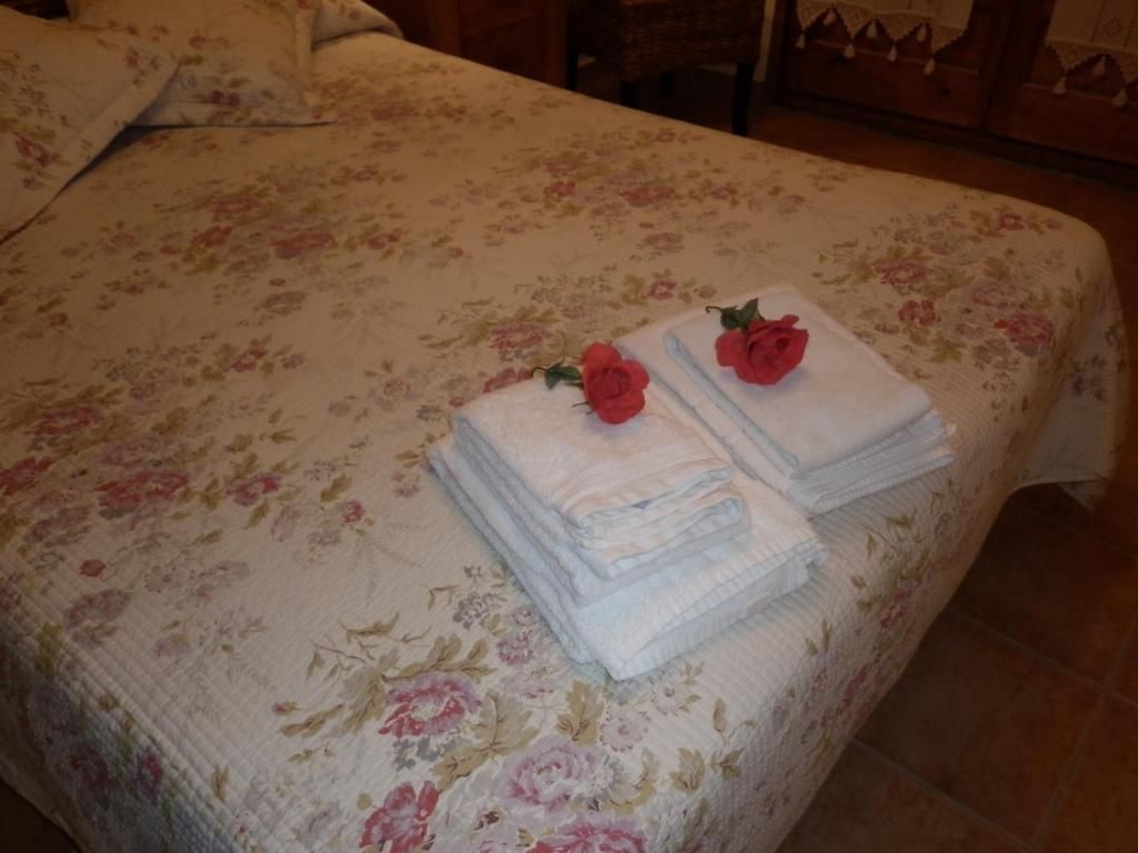 Llit amb edredó floral, tovalloles blanques plegades amb flors vermelles a la part superior.