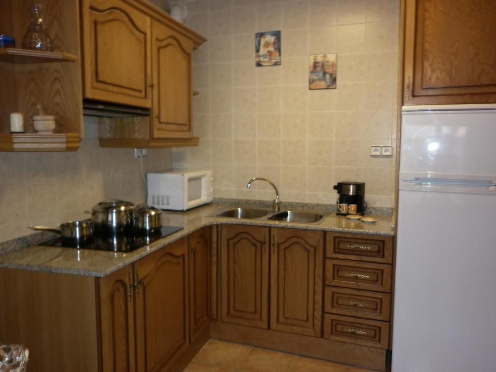 Una cuina amb armaris de fusta, taulells de granit i pica d'acer inoxidable. Inclou microones, fogons i nevera.