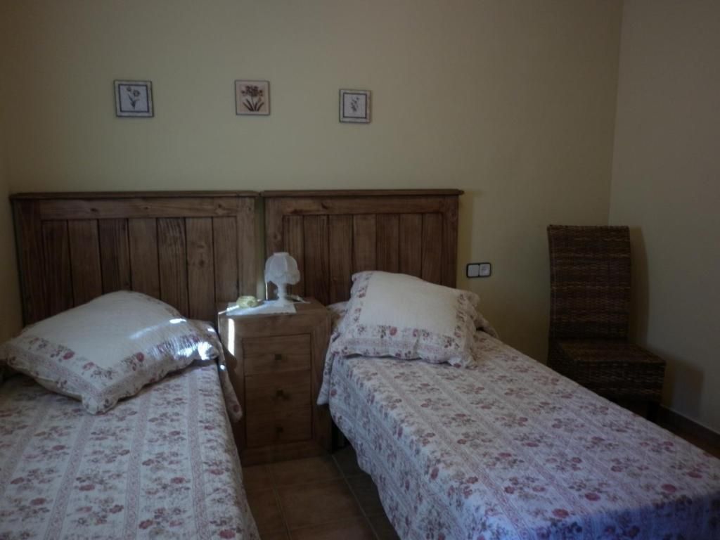 Dos llits individuals amb capçals de fusta, tauleta de nit, coixins decoratius, cobrellits florals i una cadira.