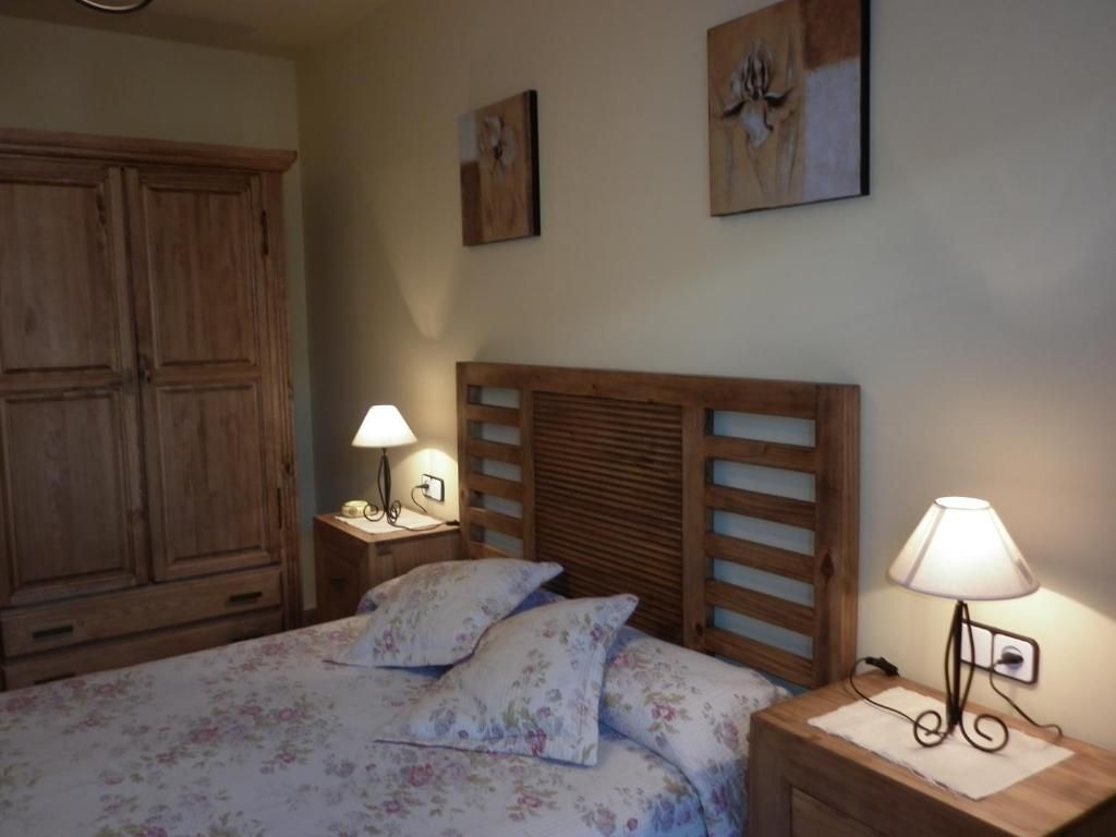 Dormitori amb mobles de fusta, llit amb roba de llit floral, tauletes de nit, làmpades, obres d'art i un armari.