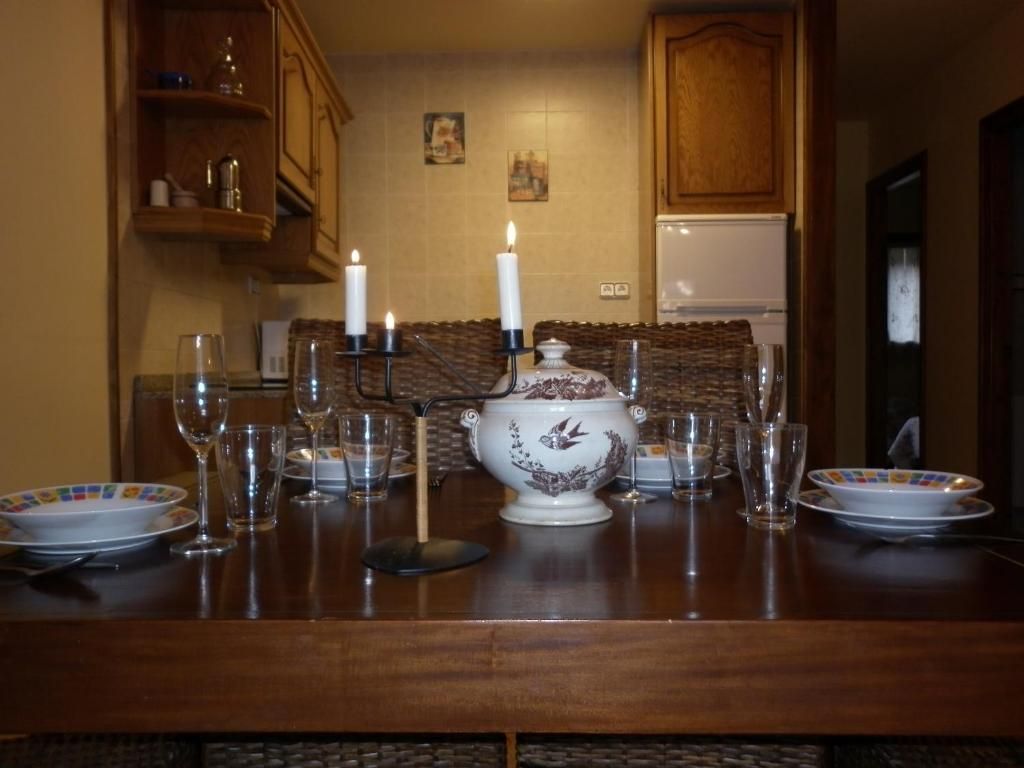 Taula de menjador parada per a un àpat amb espelmes enceses, plats, gots i una sopera en una cuina.