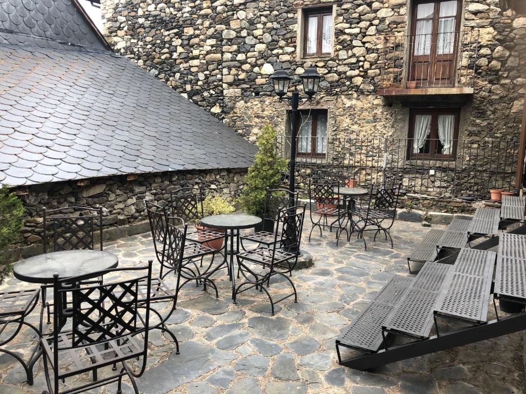 Pati exterior amb taules i cadires, parets de pedra i sostre metàl·lic.