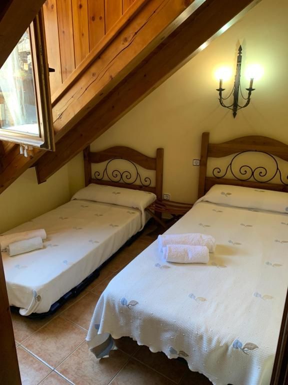 Dos llits individuals en una habitació amb sostre inclinat i bigues de fusta. Es veu una finestra a l'esquerra.