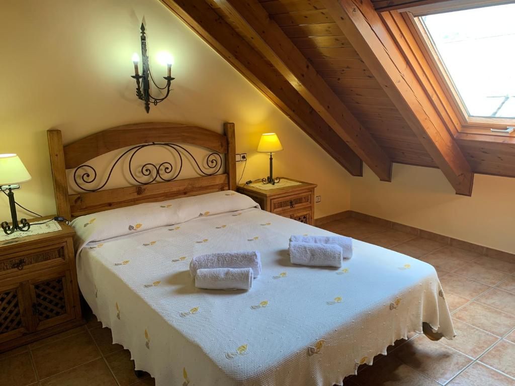 Dormitori amb llit de fusta, tauletes de nit, sostre inclinat i claraboia.