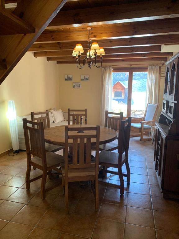 Menjador amb taula rodona, sis cadires, bigues de fusta, llum de sostre, finestra amb vistes.