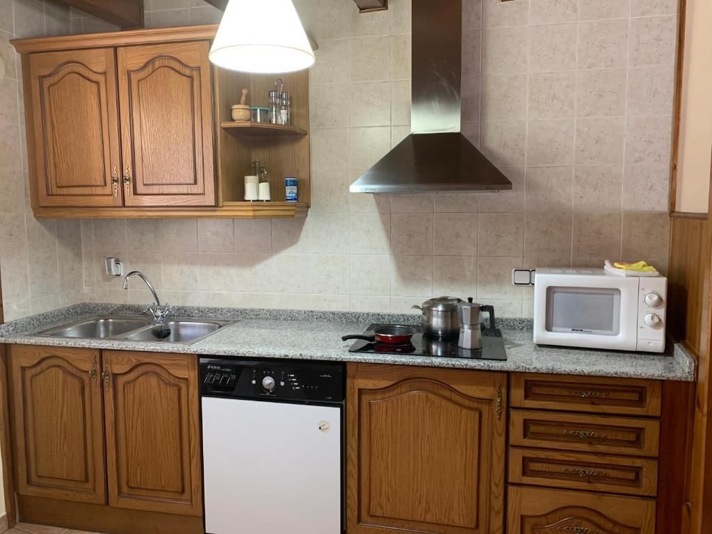 Cuina amb armaris de fusta, taulells de granit i campana extractora d'acer inoxidable. Inclou pica, fogons, microones i rentaplats.