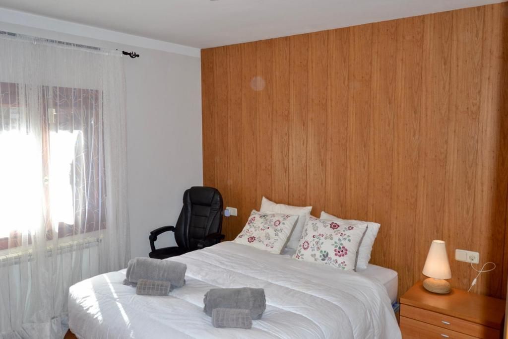 Dormitori amb capçal de fusta, llit doble amb roba de llit blanca i cadira d'escriptori.