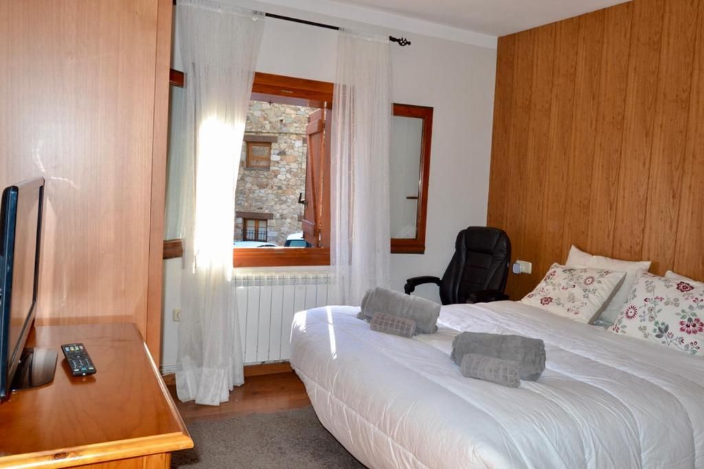Dormitori amb llit doble, TV, revestiment de fusta i finestra amb vistes a una paret de pedra.