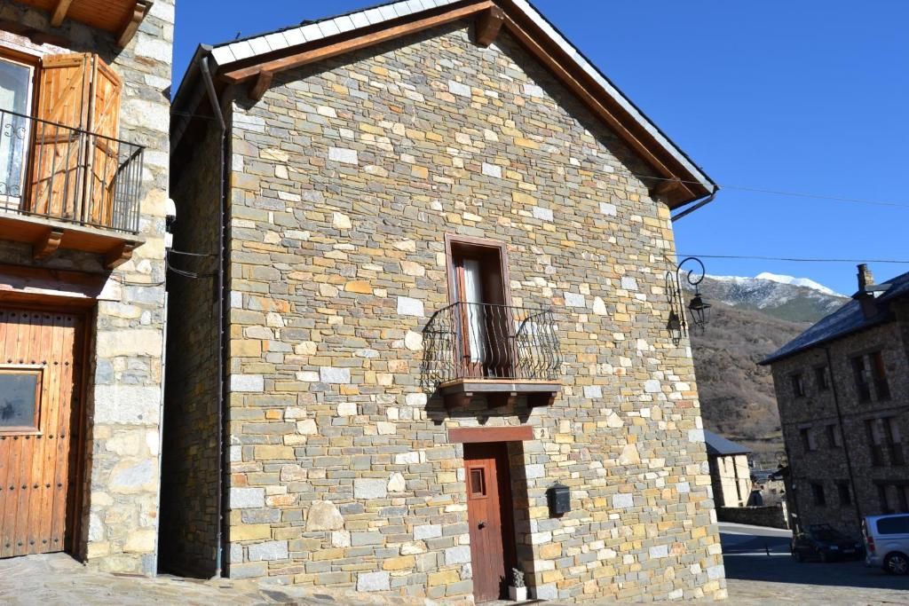 Edifici de pedra amb porta i balcó de fusta, cel blau, muntanya al fons.