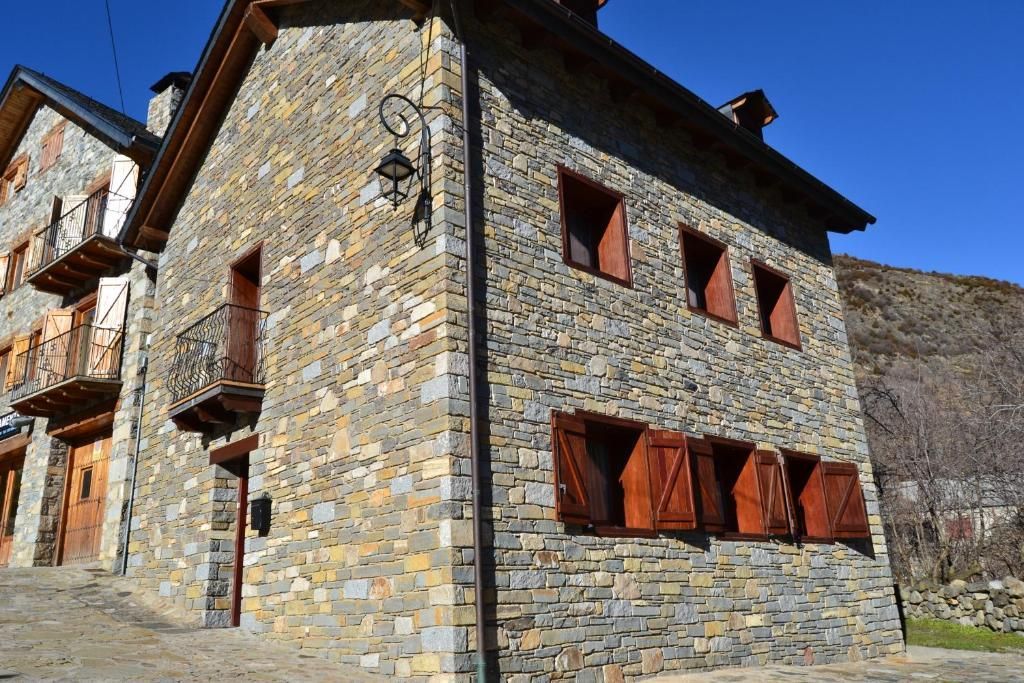 Edifici de pedra amb persianes marrons i un petit balcó en un poble, sota un cel blau.