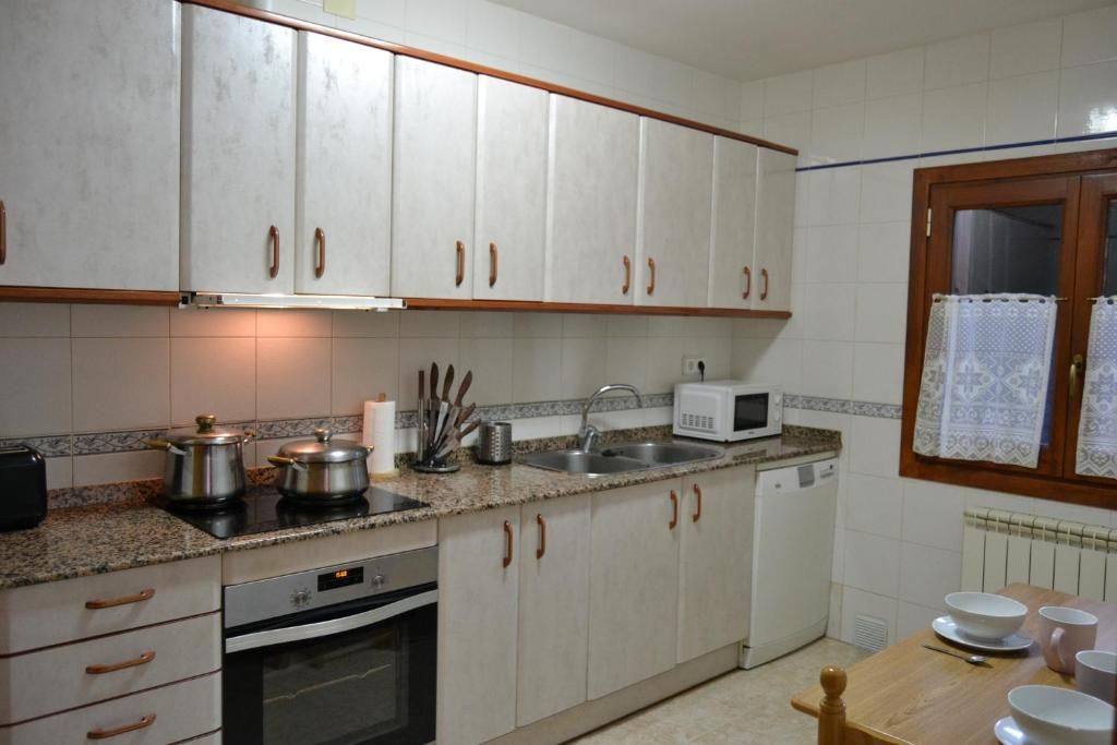 Cuina amb armaris blancs, taulell de granit, forn, pica i microones. Finestra a la dreta.