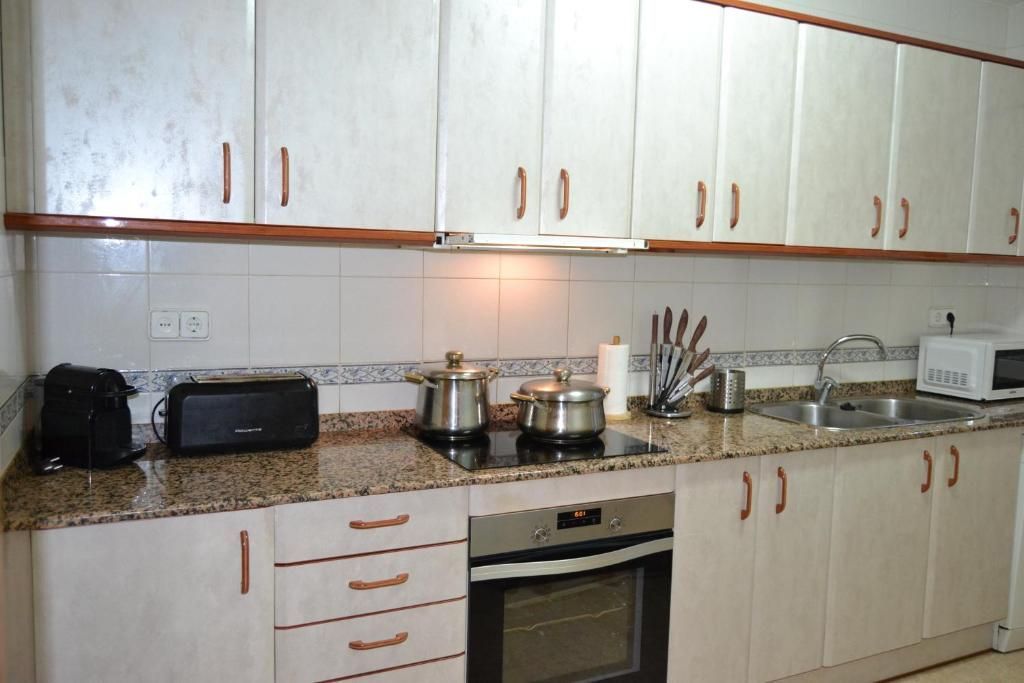 Cuina amb armaris blancs, taulells marrons i electrodomèstics d'acer inoxidable.