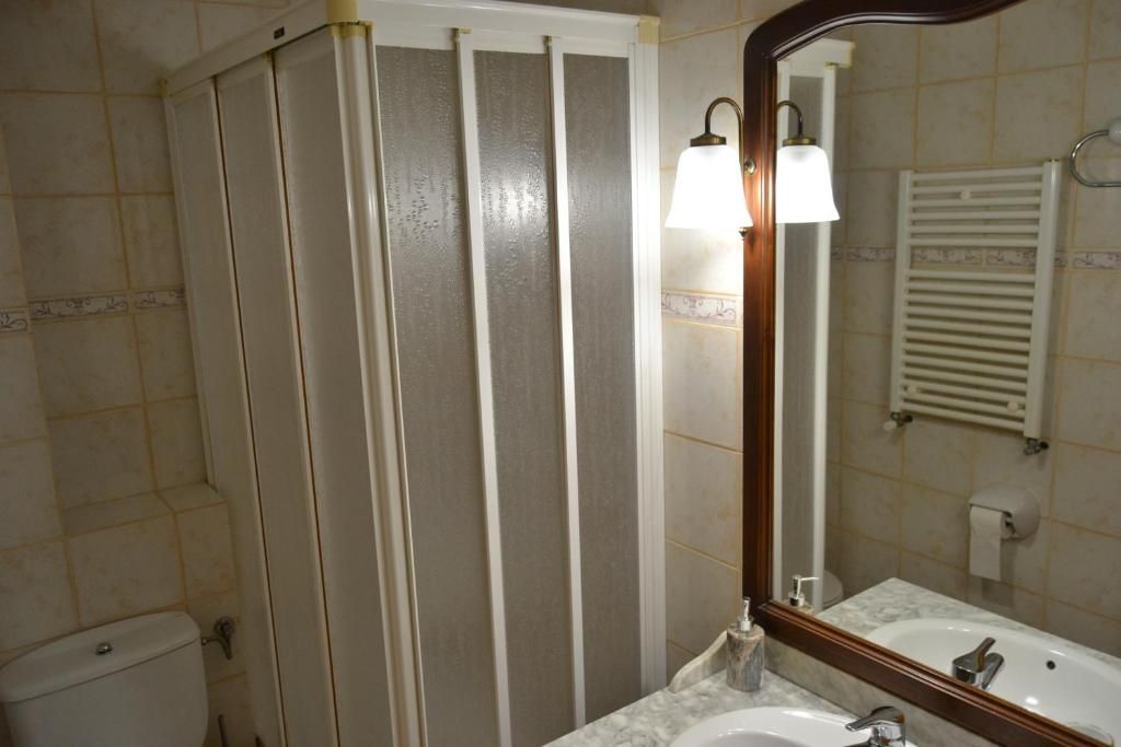 Bany amb cabina de dutxa plegable blanca, vàter, lavabo amb mirall i escalfador de tovalloles.