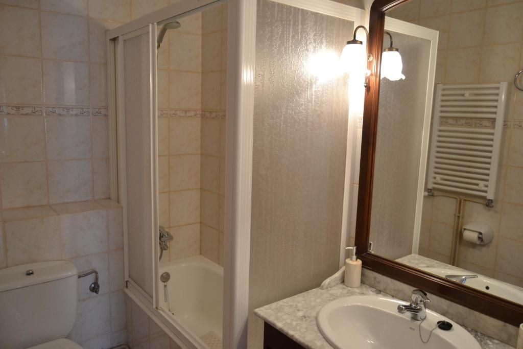 Bany amb dutxa/banyera, vàter, lavabo, mirall i tovalloler. Tons blanc trencat i marrons.