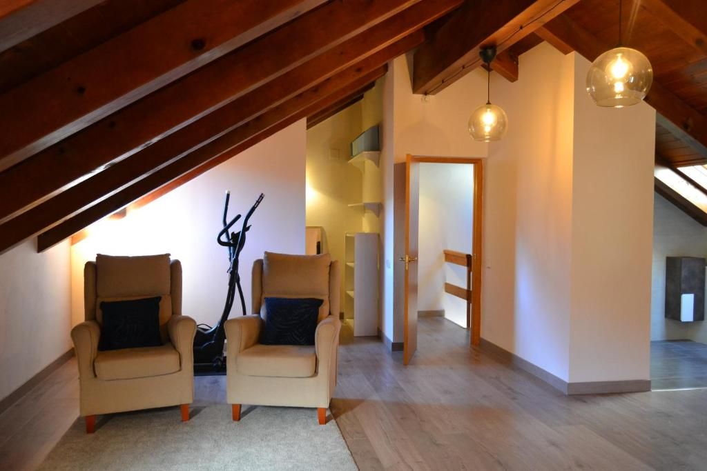 Zona d'estar a les golfes amb dues butaques, bigues de fusta, llums penjants i porta.