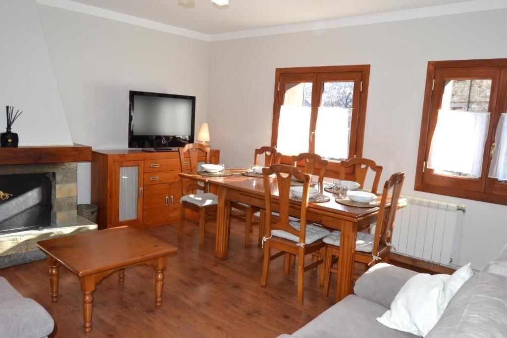 Sala d'estar amb menjador: mobles de fusta, llar de foc, grans finestrals, TV, sofà i taula de menjador per a sis persones.