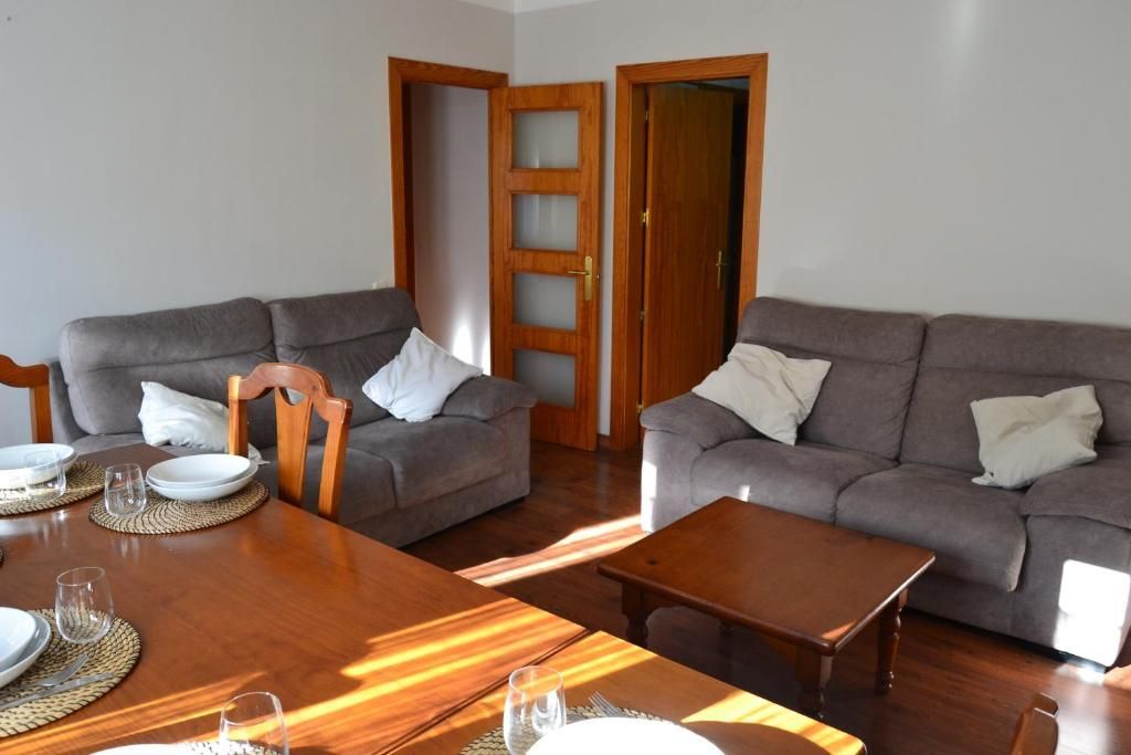 Sala d'estar amb sofàs marrons, taula i portes de fusta; la llum del sol entra a raig.