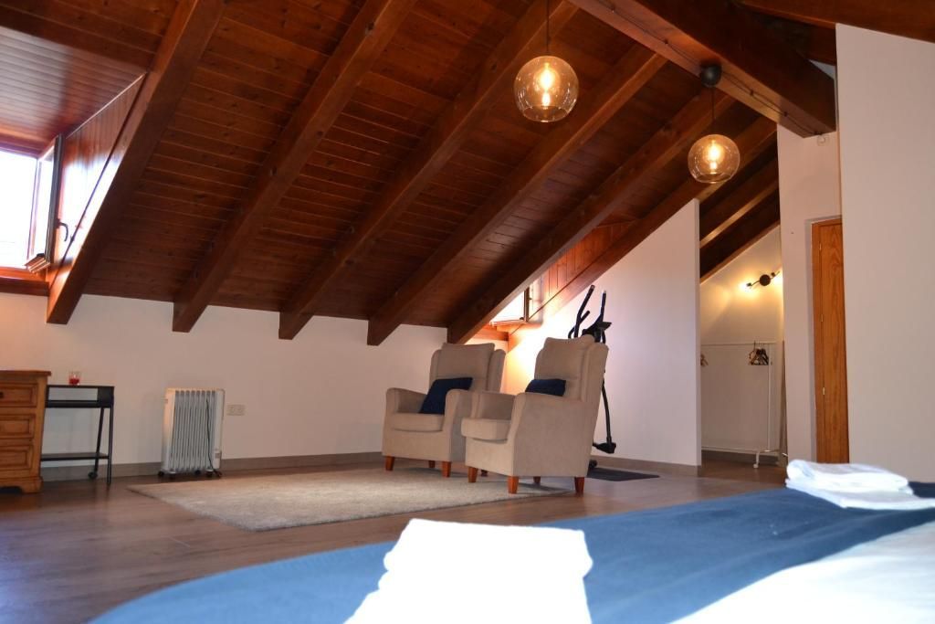 Dormitori a les golfes amb sostre de fusta, dues butaques, llit i un petit calefactor. Il·luminació càlida.
