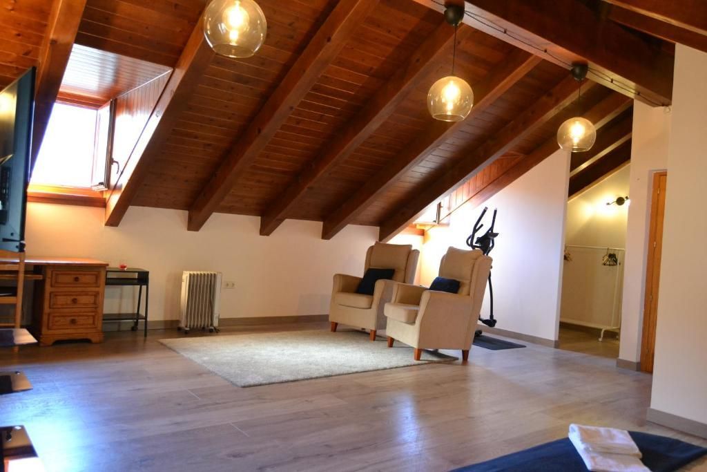 Sala d'estar a les golfes amb bigues de fusta, claraboia, butaques, catifa i llums penjants.